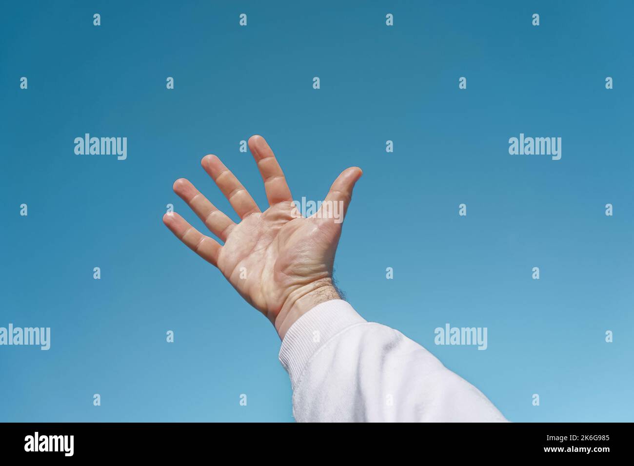 mano in su nell'aria gesturing nel cielo blu, fondo blu Foto Stock