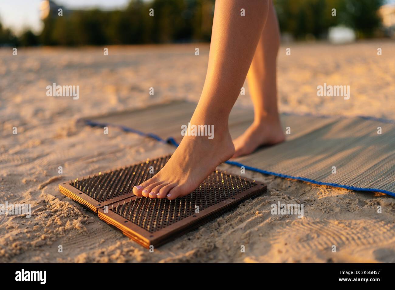 Piedi ravvicinati di una donna irriconoscibile che sale sul bordo del chiodo di Sadhu durante la pratica di meditazione di concentrazione sulla spiaggia sabbiosa del mare alla mattina di sole di estate Foto Stock