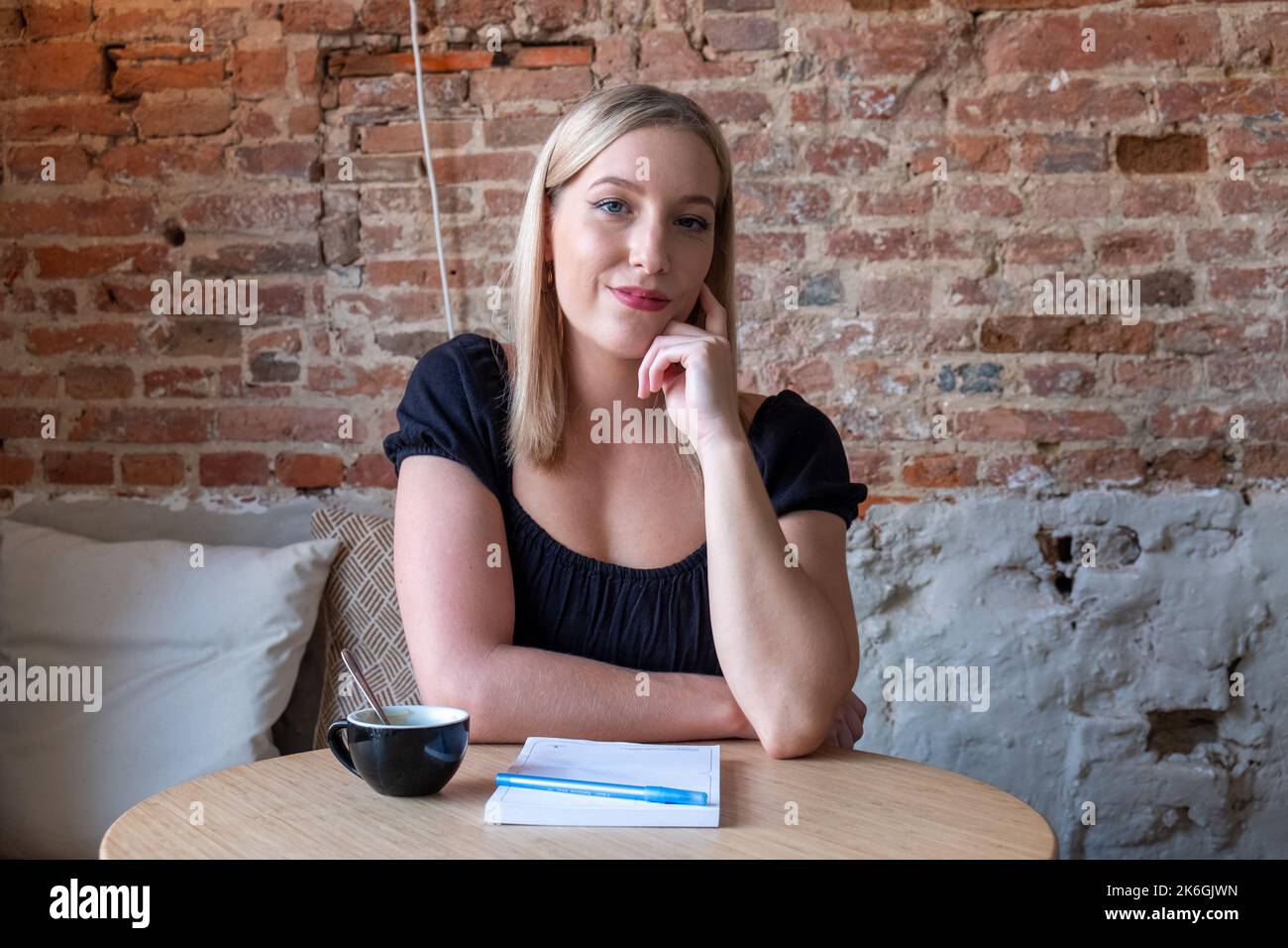 Giovane donna sognante scrivere piani futuri e obiettivi nel proprio diario che riposa in una caffetteria accogliente con tazza di gustoso cappuccino.smiling ragazza hipster facendo ottenere buona idea mentre scrive in blocco note. Foto di alta qualità Foto Stock