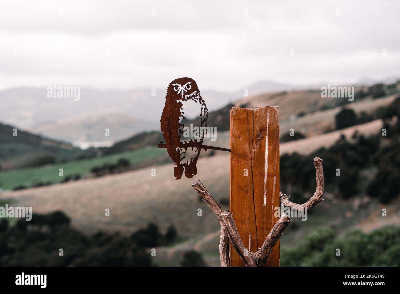 scultura in metallo a forma di gufo inchiodato a un palo di legno che domina la valle circondata da alberi di montagna e la natura in un luogo tranquillo vicino Foto Stock