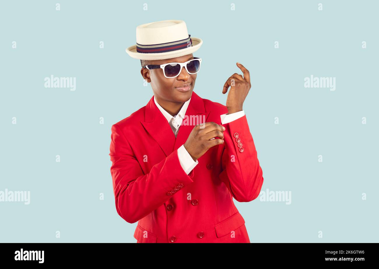 Giovane uomo afroamericano alla moda in tuta rossa e cappello in piedi in uno studio blu pastello Foto Stock