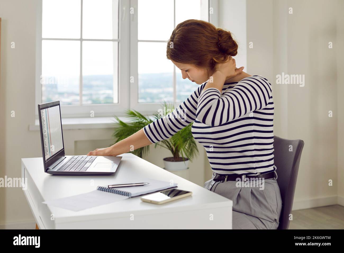 Donna stanca e stressata con dolore al collo che lavora su un computer portatile alla scrivania dell'ufficio Foto Stock