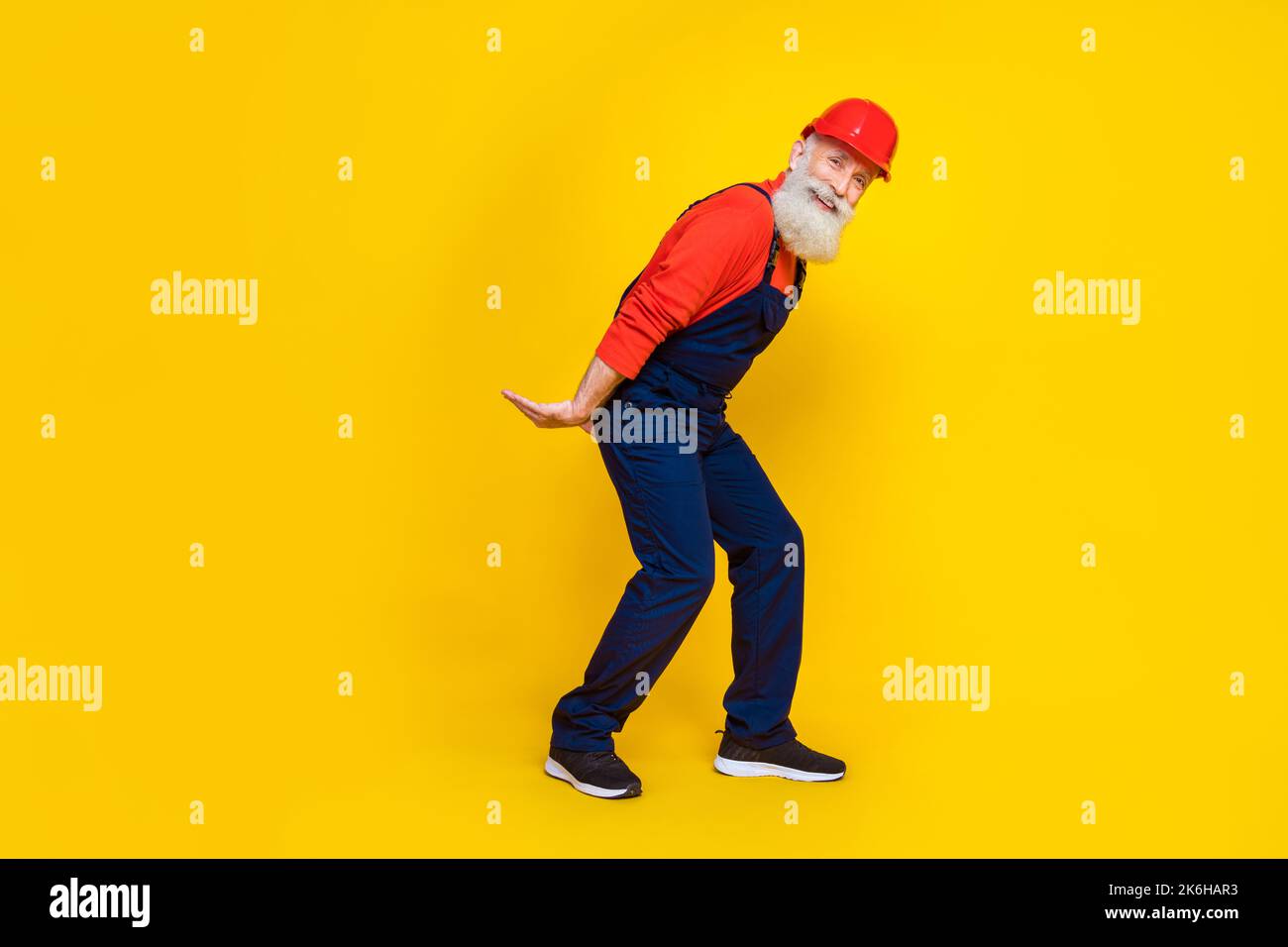 Foto a tutta lunghezza di un caposquadra positivo ottimista con barba bianca e casco rosso resistenza peso pesante isolato su sfondo giallo Foto Stock