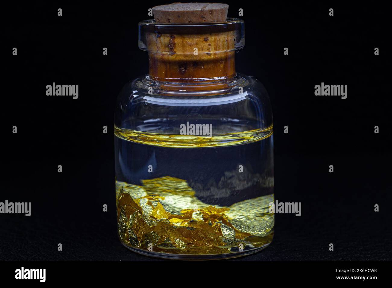 Una piccola bottiglia di vetro con un sughero di legno su una superficie nera con oro Carat 22 lascia macro primo piano Foto Stock