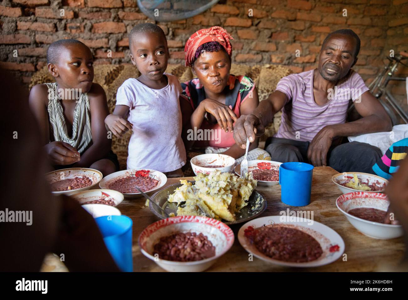 Famiglia ugandese che condivide un pasto a base di fagioli e purè di banane saporite nella loro casa nel distretto di Kasese, Uganda, Africa orientale. Foto Stock