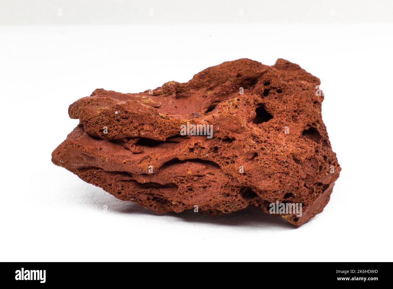 Rosso ruvido pietra lavica macro focalizzata e isolata su superficie bianca macro isolata Foto Stock