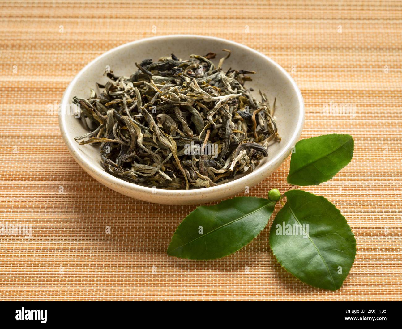 Ciotola con Bai Mao Hou, foglie di tè essiccate di scimmia bianca, primo piano e foglie di tè verde fresco Foto Stock