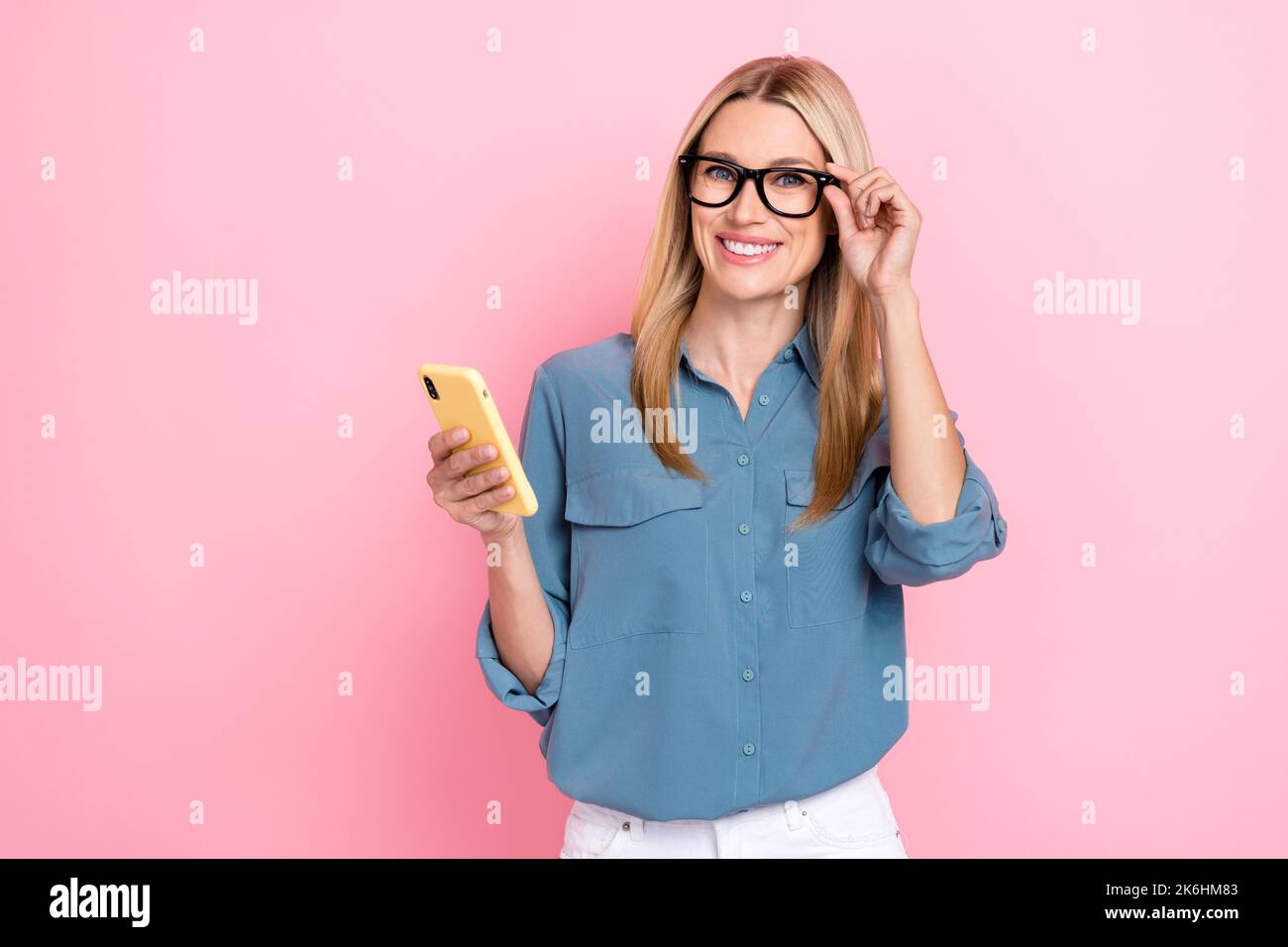 Ritratto foto di maturo sicuro successo pretty bello imprenditore donna indossare occhiali tenere telefono buona visione controllo isolato sul colore rosa Foto Stock
