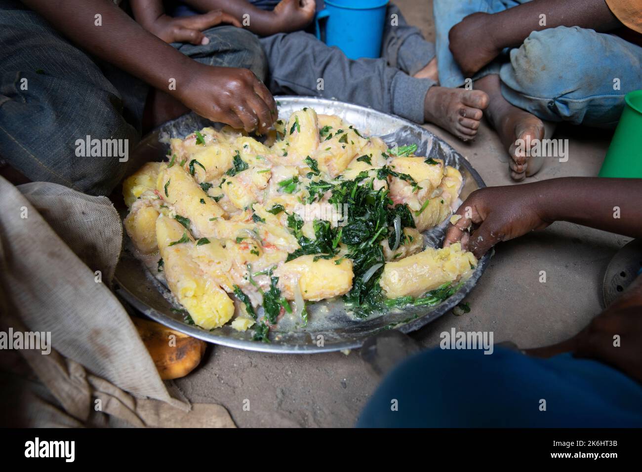 Un gruppo di bambini africani mangia un pasto a base di banane e verdure con salsa di arachidi nella loro casa nel distretto di Kasese, Uganda, Africa orientale. Foto Stock