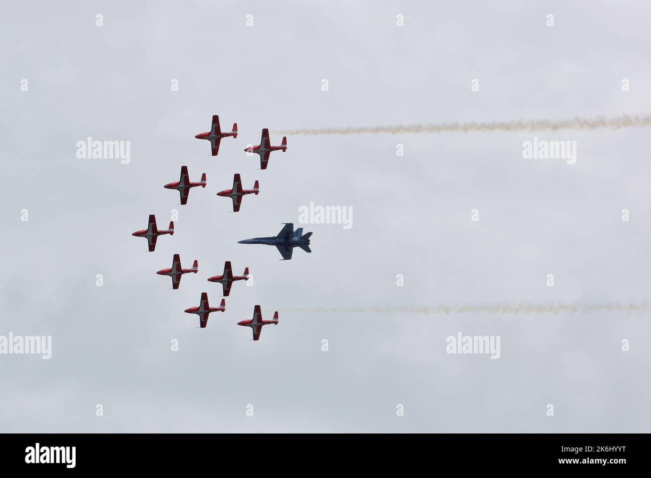 RCAF Snowbirds che volano in formazione, insieme ad un jet da caccia. Due flussi di fumo su entrambi i lati della formazione. Foto Stock