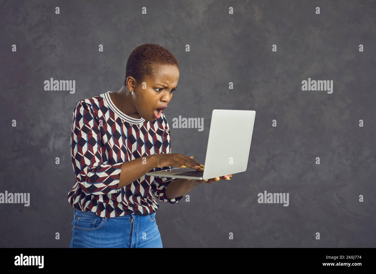 Giovane afroamericana con faccia scioccata e sorpresa guardando lo schermo del laptop. Foto Stock