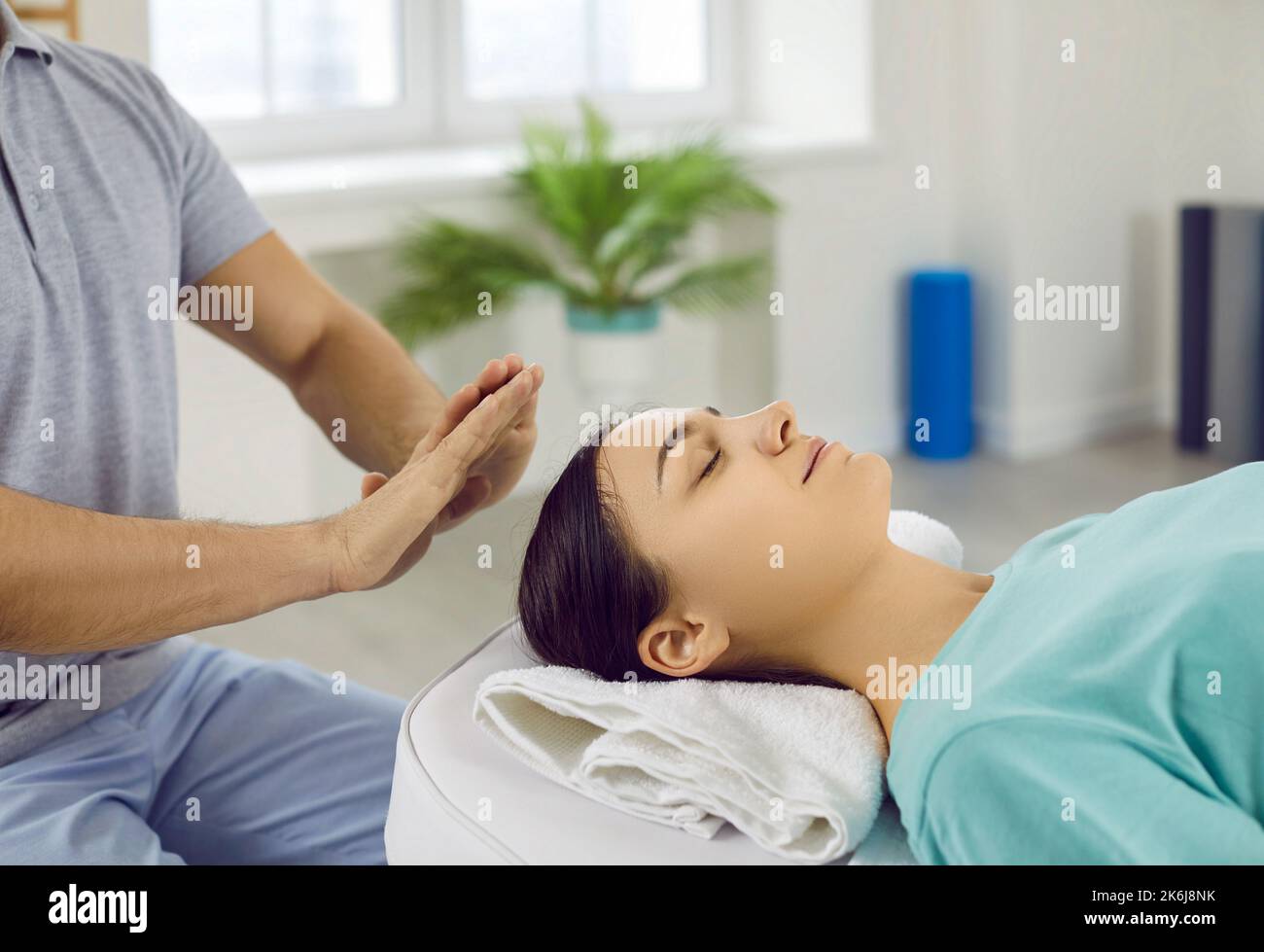 Giovane donna che si rilassa e ripristina energia durante la sessione di terapia con il guaritore Reiki Foto Stock