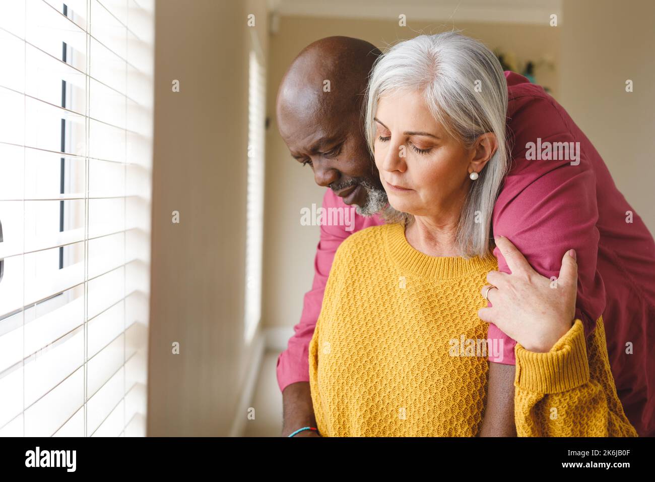 Premuroso, triste coppia anziana diversa abbracciando e guardando giù a casa Foto Stock