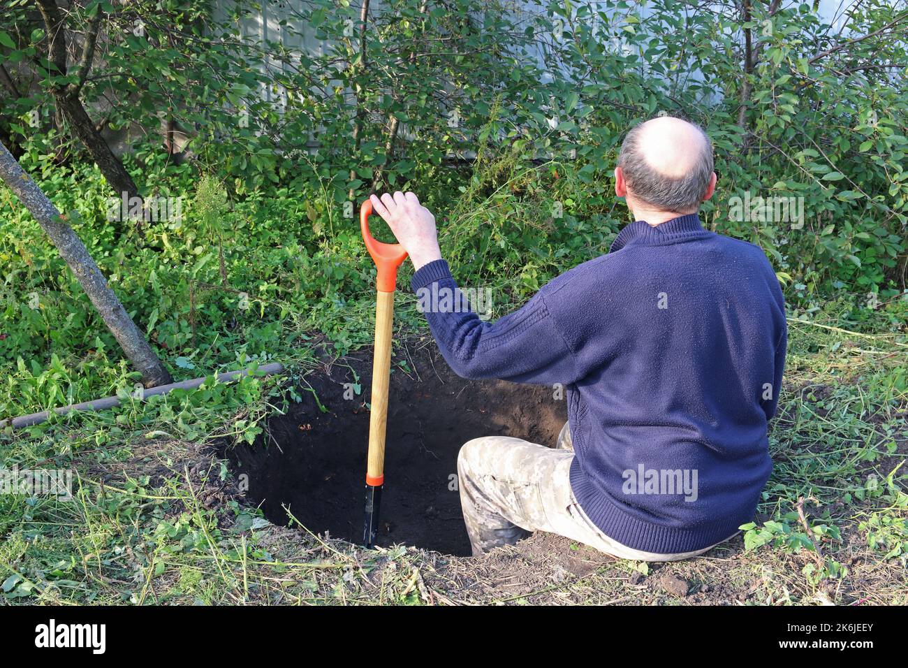 L'uomo scava una buca profonda. L'uomo si riposa dopo il lavoro. Scavando una buca da pala. Foto Stock