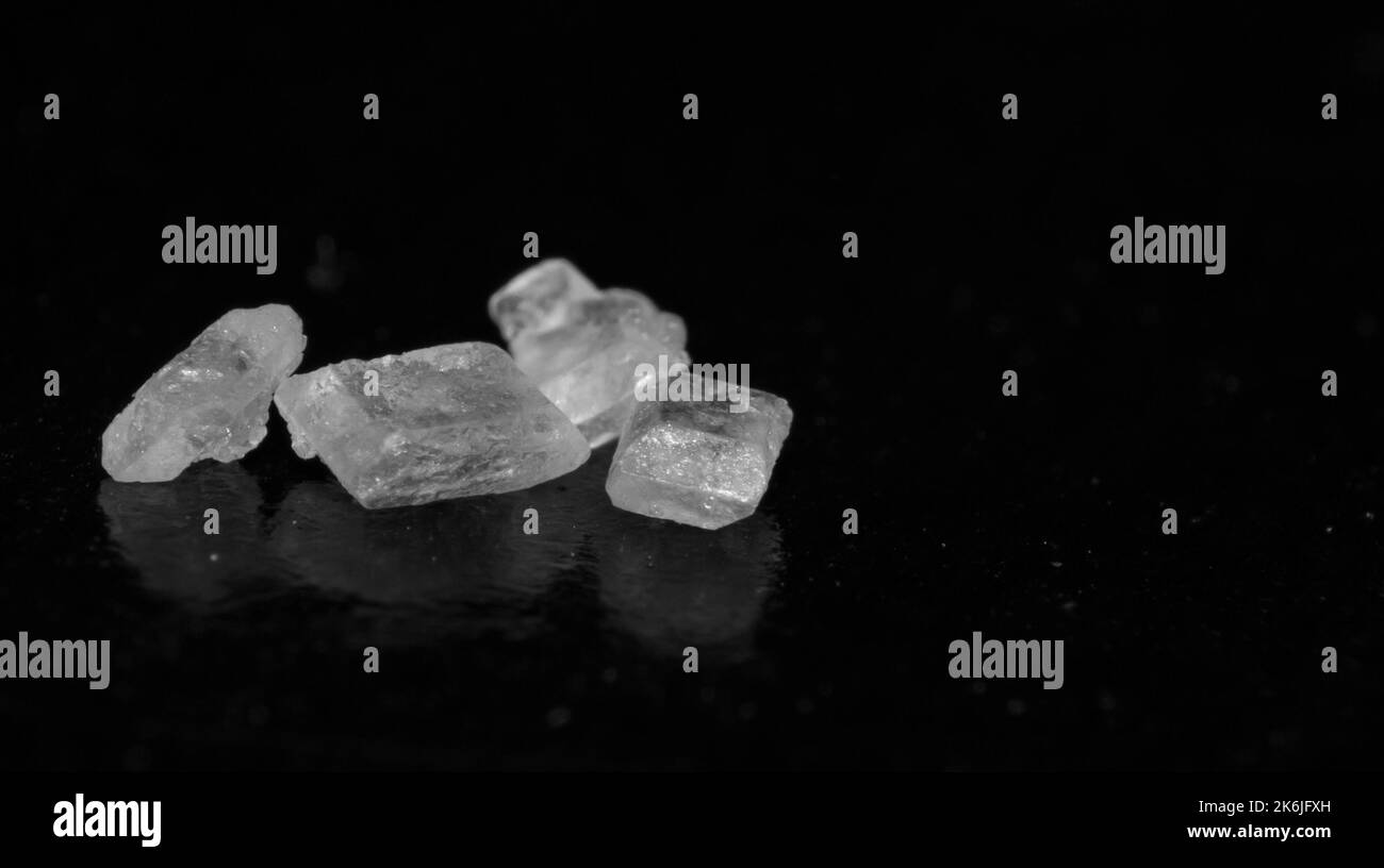 Macro immagine dei cristalli di zucchero bianco su sfondo nero e messa a fuoco selettiva. Immagine ravvicinata dei chicchi di zucchero bianco. Foto Stock