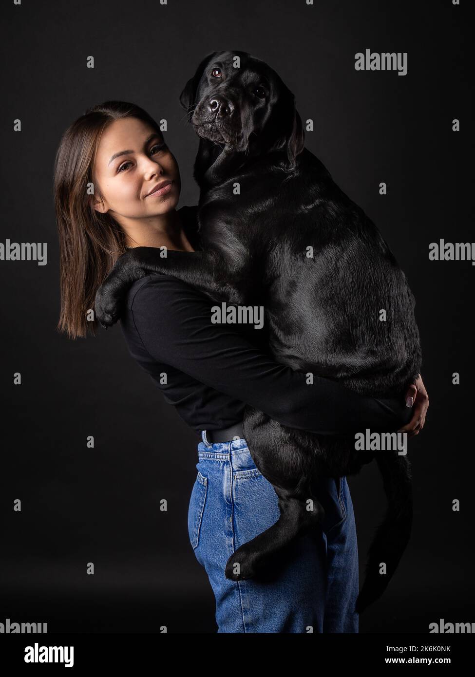 Una ragazza tiene un cane Labrador Retriever tra le braccia. Scattato in primo piano in uno studio fotografico, su sfondo nero. Foto Stock
