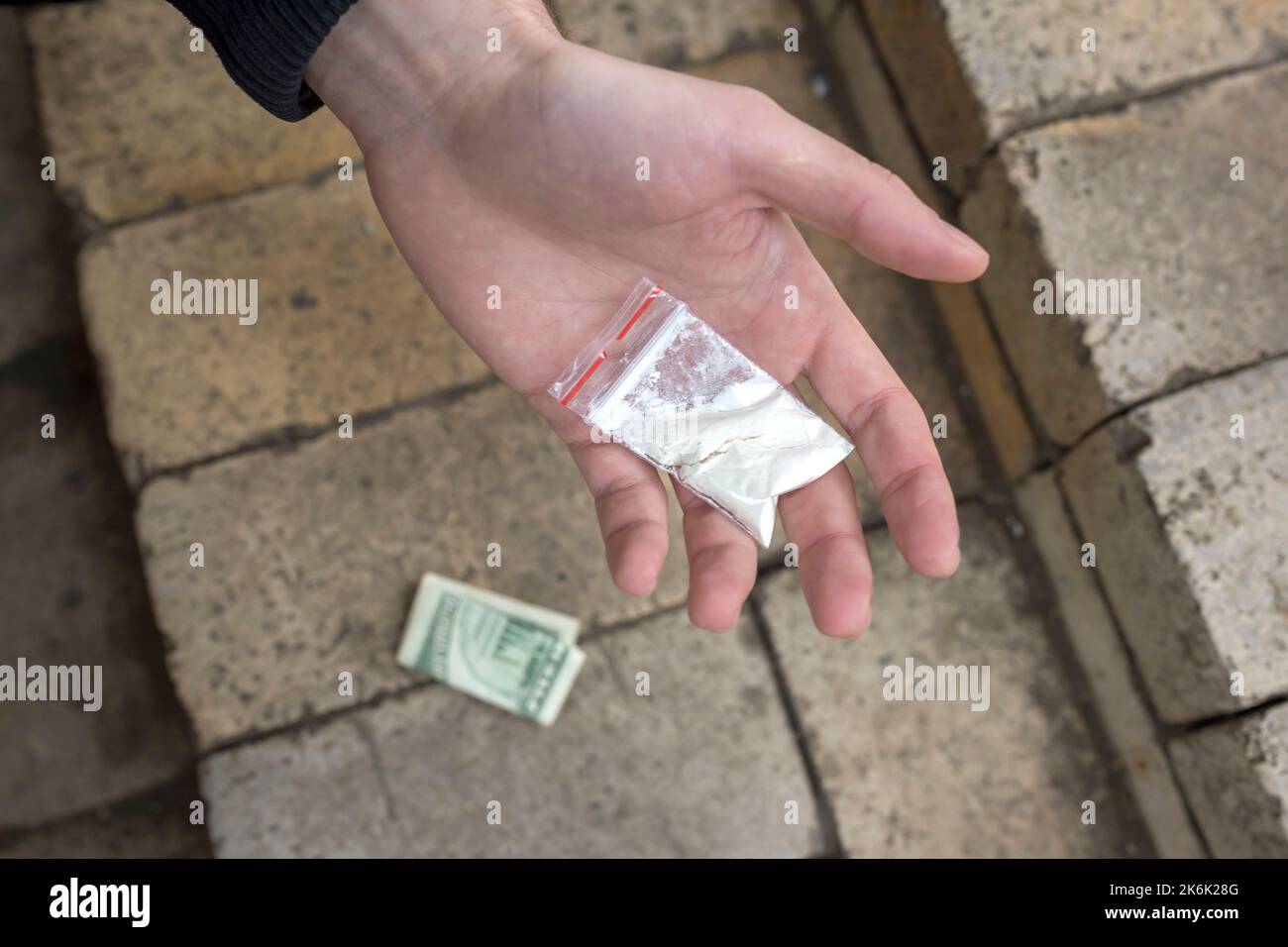 Mano di un dipendente che tiene una busta di plastica nel palmo con polvere di cocaina o altre droghe. Primo piano. Concetto di dipendenza. Foto Stock