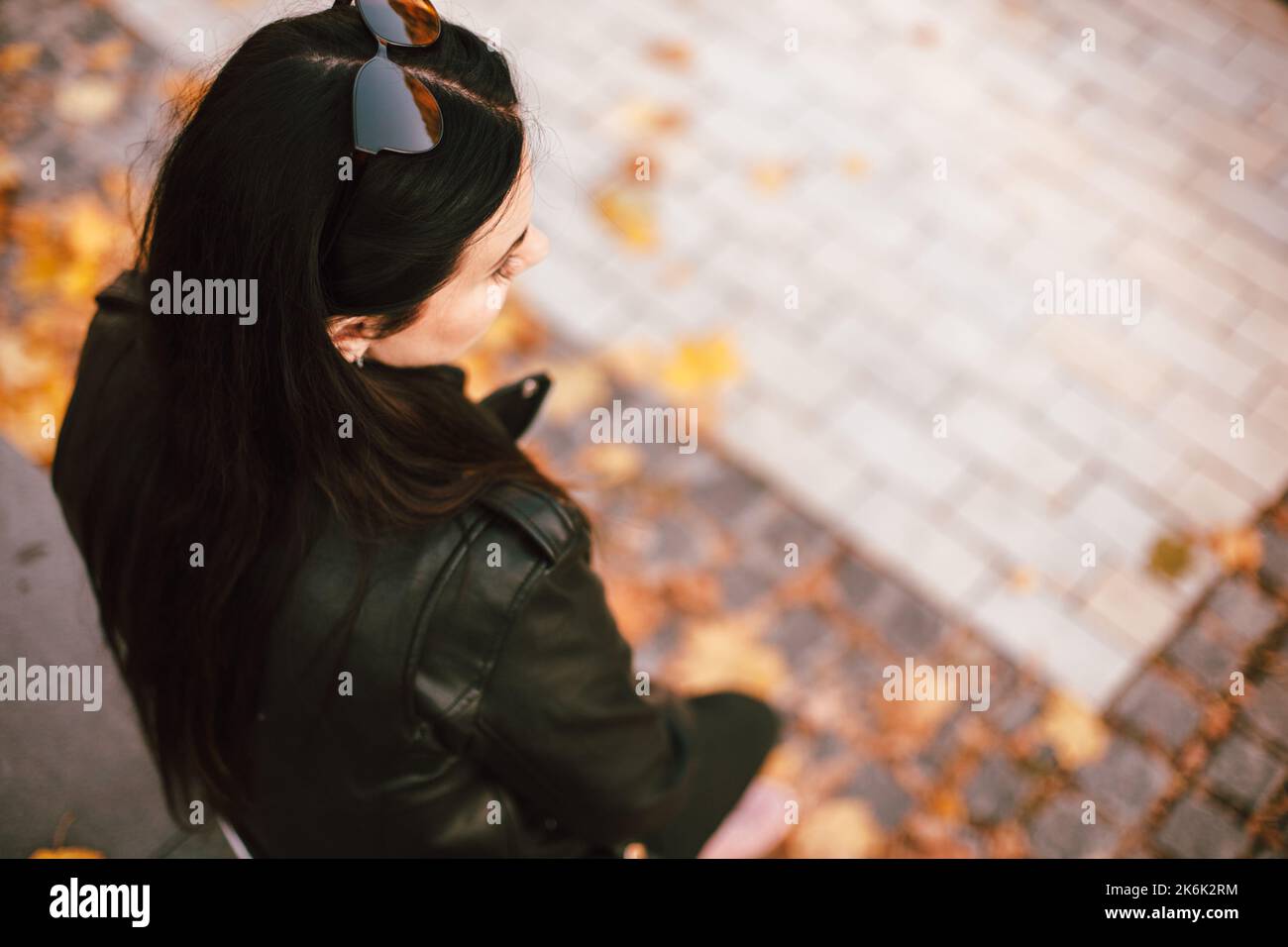 Vista ad alto angolo della giovane donna alla moda e premurosa che indossa occhiali da sole sulla testa seduta nel parco in autunno Foto Stock