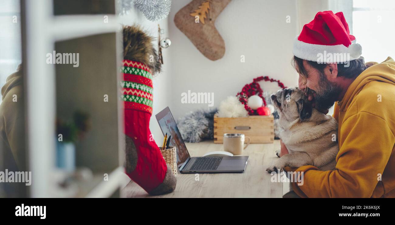 Festa di Natale a casa con un solo uomo in videoconferenza su laptop abbracciando il suo adorabile cane animale domestico. Concetto di persone che godono dee Foto Stock