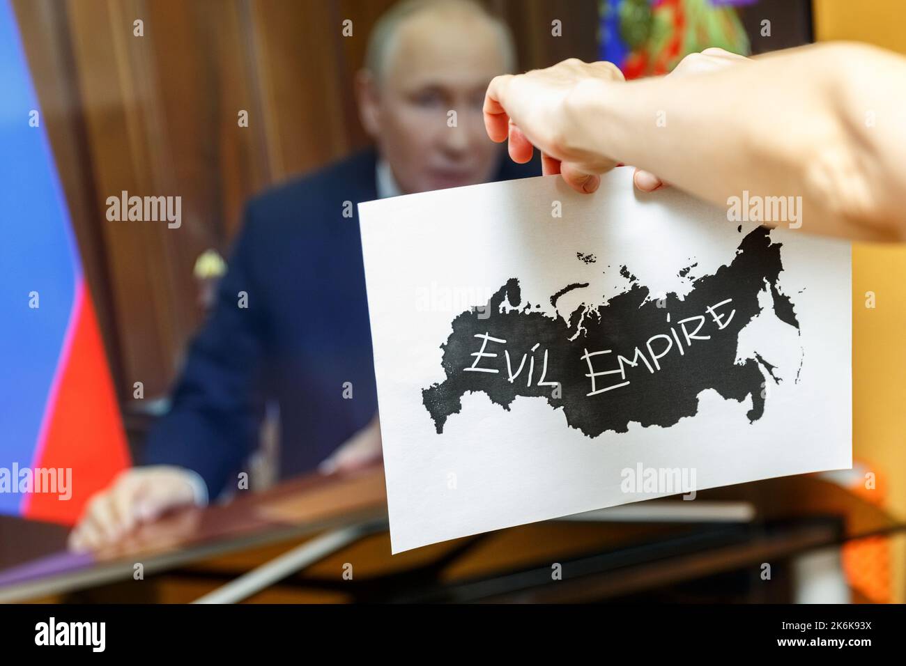 Mani strappare carta con contorni neri della Russia con una frase Evil Empire scritto su di esso, di fronte a un tv set.Russia disintegrazione concetto Foto Stock