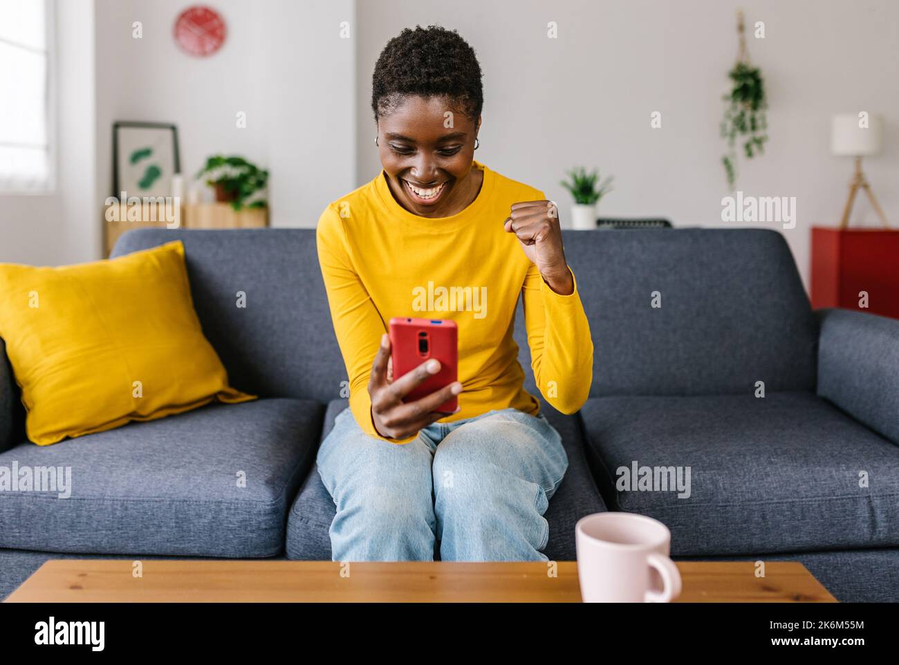 Giovane donna africana eccitata che celebra il successo tenendo il telefono cellulare Foto Stock
