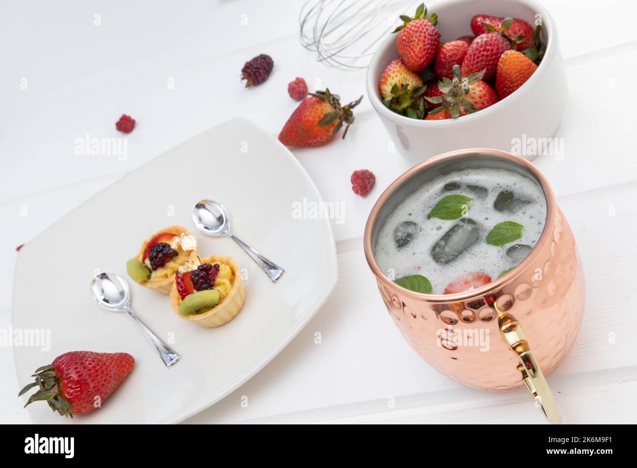 decorazione al tavolo servita con due torte, fragole e un bicchiere con bevanda fredda, cibo delizioso e appetitoso come spuntino in studio Foto Stock