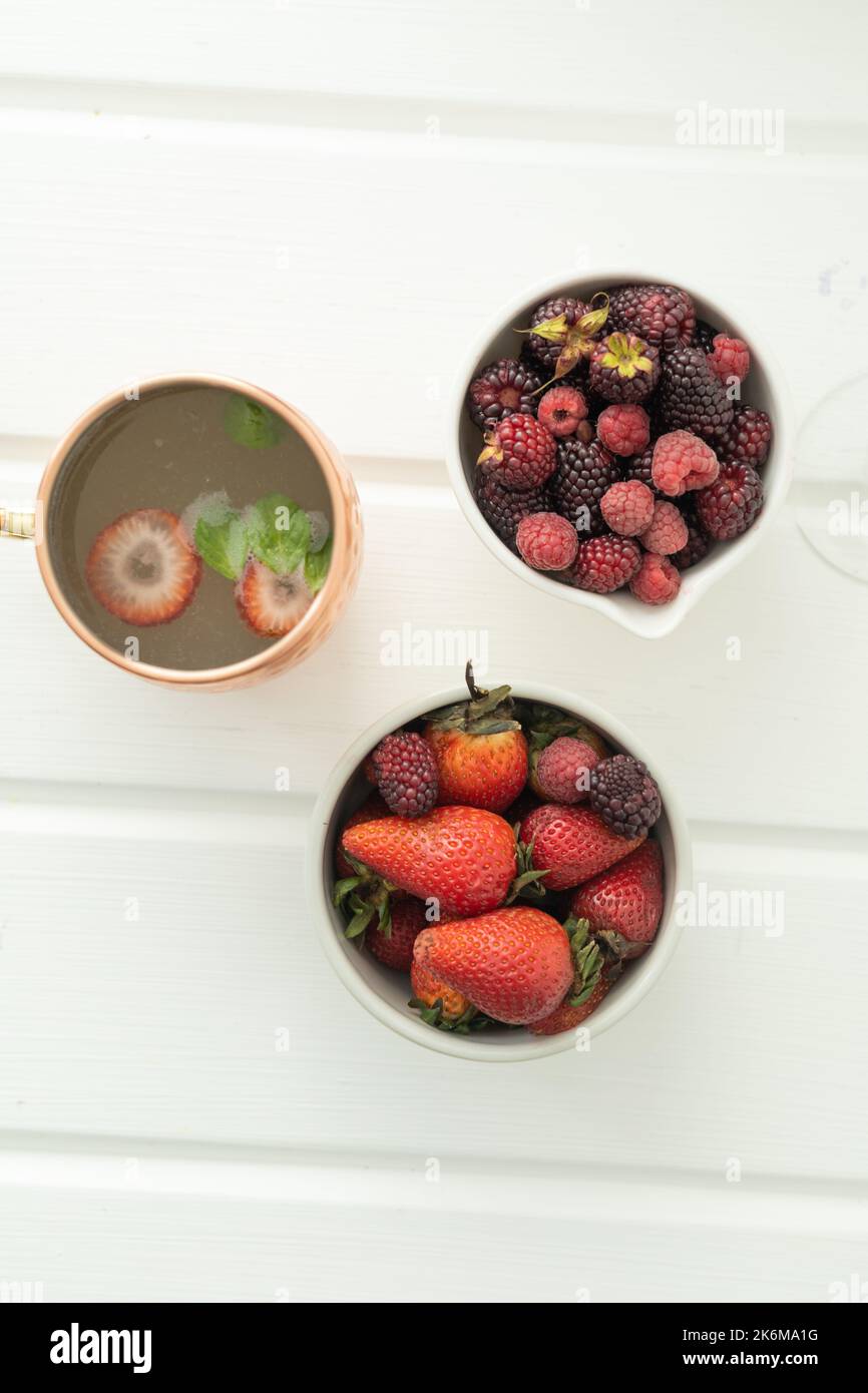 tavolo decorato con frutti di bosco freschi, fragole e more, mangiare sano con un bicchiere di bevanda fredda, prospettiva dall'alto Foto Stock