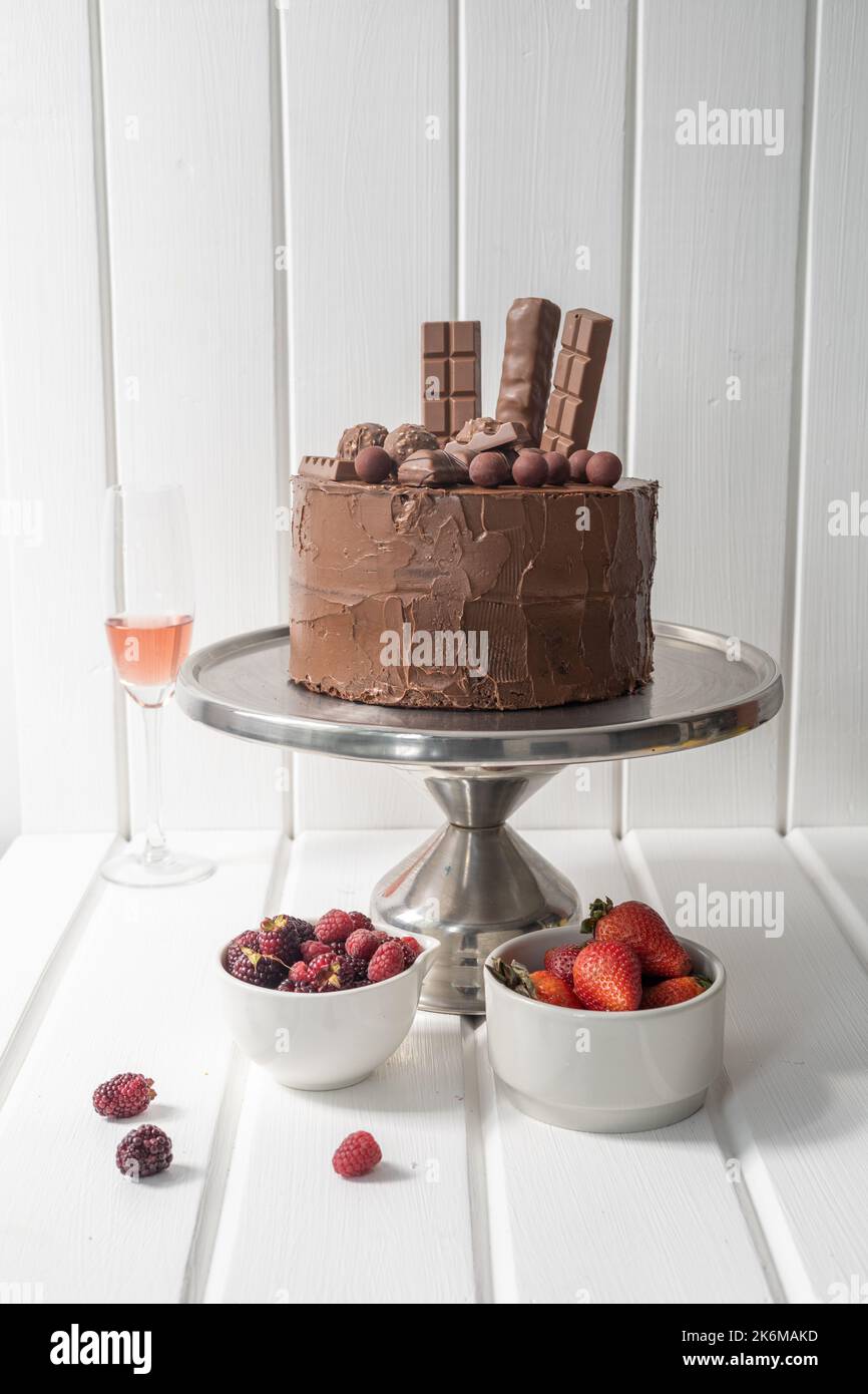 decorazione di torta al cioccolato con cioccolatini su un piatto laterale con frutta e una tazza di vetro, tavolo pronto per la festa, pasticceria in studio Foto Stock