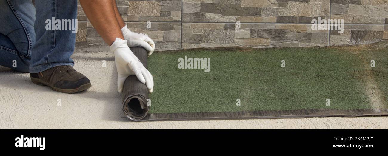 Operai edili che srotolano la guaina bituminosa tardata per l'isolamento e la protezione di tetti e pavimenti dalla pioggia e dalle intemperie. Handyman Foto Stock