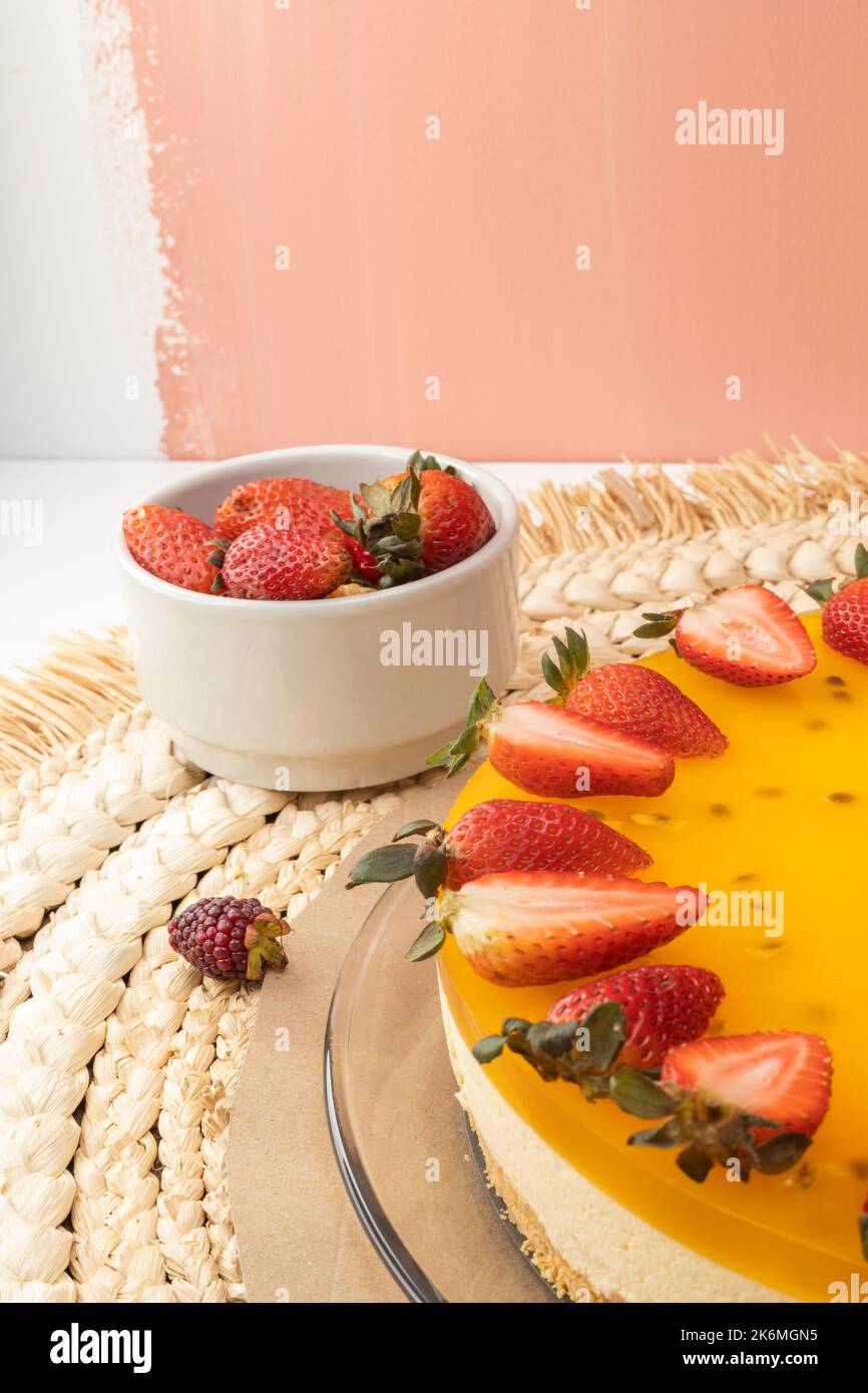 monolocale con cheesecake alla frutta della passione con crema decorata con fragole, dolce cibo gourmet, tavolo servito e frutta accanto ad esso Foto Stock