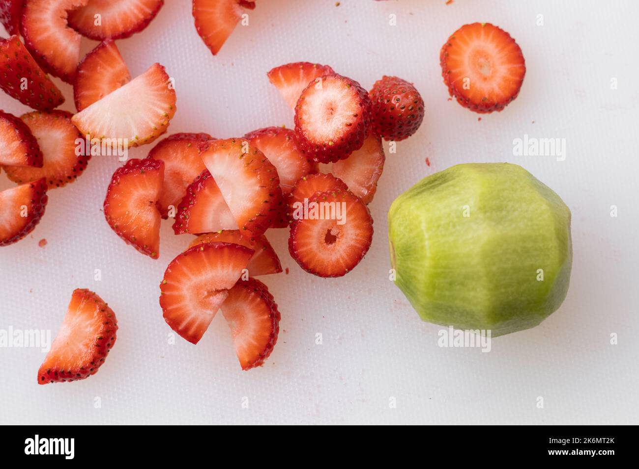 fragola tagliata a pezzi, frutta tropicale come ingrediente alimentare accanto a un kiwi pelato, preparazione alimentare Foto Stock