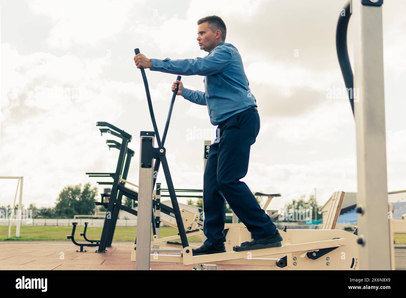 Un uomo in tuta da lavoro si sta riscaldando sui simulatori dello stadio. Esercizi sportivi dopo il lavoro d'ufficio. La lotta contro l'eccesso di peso. Uomo d'affari Foto Stock