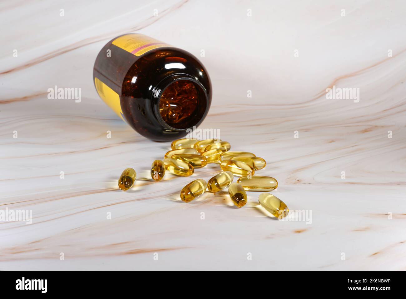Capsule di olio di pesce versate fuori contenitore aperto sul banco di marmo. Foto Stock