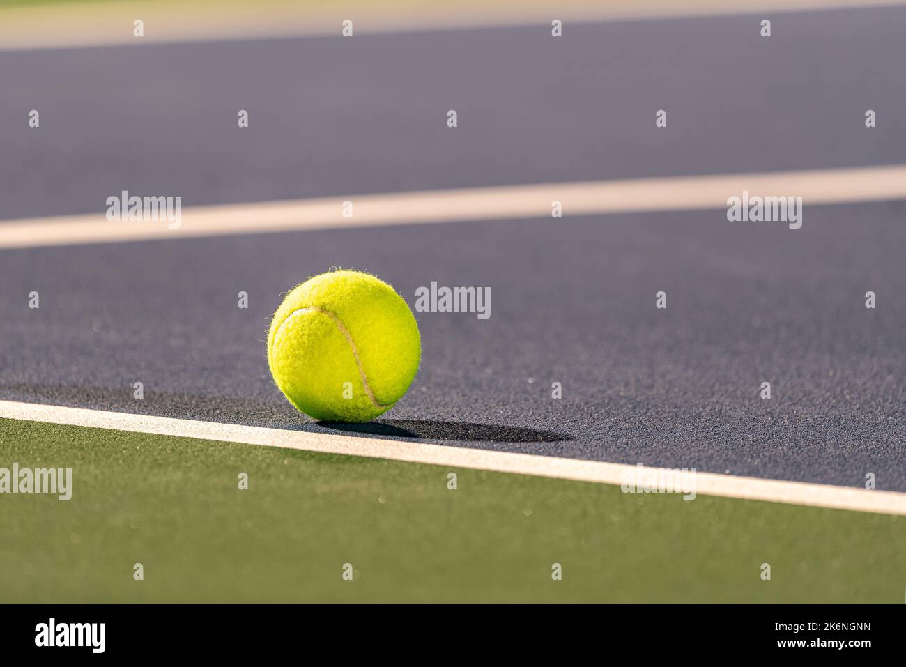 Foto scattata in tarda serata sotto le luci di una palla da tennis gialla sul campo da tennis blu con linea bianca e verde fuori limite. Foto Stock