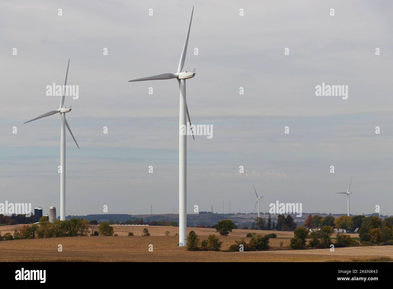 Le turbine eoliche sono visibili in una zona rurale in una giornata nuvolosa; le fattorie e i silos possono essere visti sullo sfondo. Foto Stock