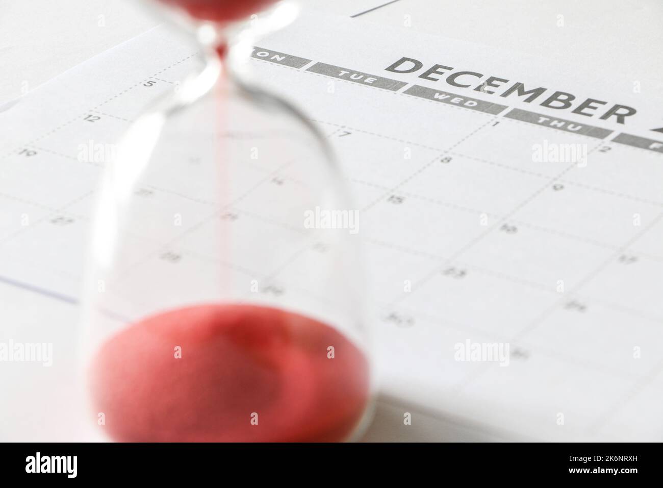 Concetto di esaurimento del tempo, calendario di dicembre, clessidra che si esaurisce in primo piano, ma fuori fuoco, conto alla rovescia fino alla fine dell'anno Foto Stock
