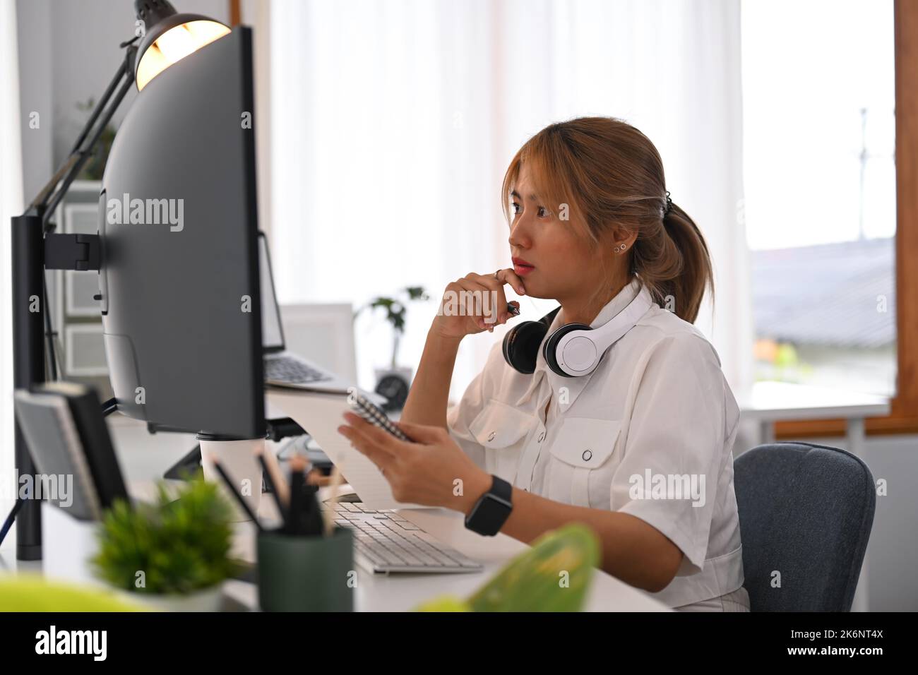 Una giovane donna concentrata che guarda lo schermo del computer, che lavora a un progetto creativo nell'ufficio domestico Foto Stock