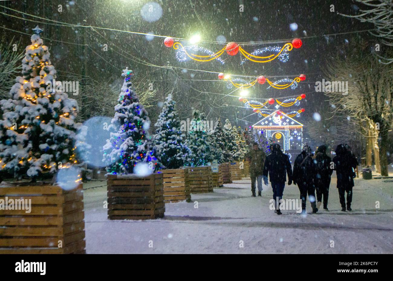 Strada cittadina durante le nevicate nella notte d'inverno. Bella illuminazione e decorazione sulla strada. Festa di Natale di Capodanno. Lanterne ghirlande sugli alberi. Foto Stock