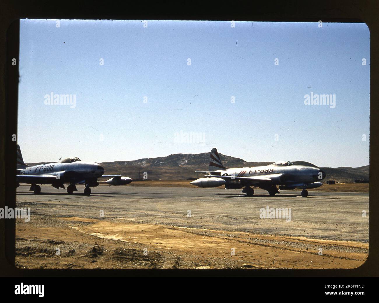 Un quarto della vista frontale destra di un Lockheed F-80 Shooting Star Taxiing, da qualche parte in Corea. L'aereo porta le marcature del 36th Fighter Bomber Squadron (FBS), e il suo numero di ronzio (FT-599) è visibile sulla fusoliera. Un'altra F-80 Shooting Star con segni simili è mostrato seguendo da vicino dietro di esso. È anche visibile il numero di ronzio (FT-606). L'apparecchiatura è visibile sullo sfondo. Foto Stock