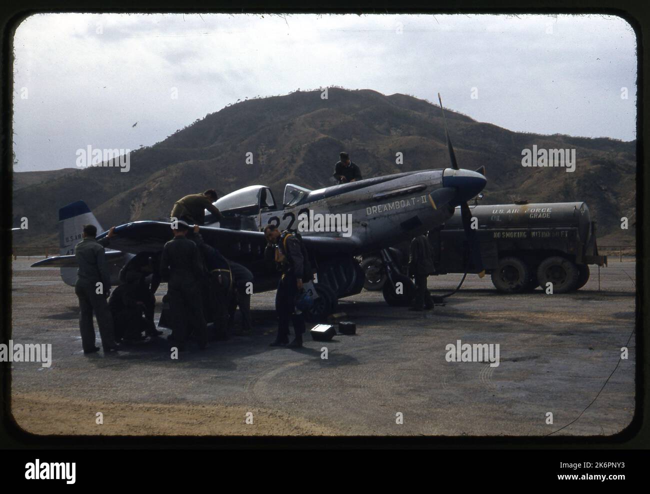 Vista frontale di un quarto di un F-51D Mustang nordamericano 'Dreamboat II' da qualche parte in Corea. Il pilota si trova sul lato destro dell'aereo e diversi equipanti lavorano sotto l'ala. Un equipaggio lavora sulla parte superiore dell'ala, e un altro si trova sull'ala sinistra che rifornisce i serbatoi dell'ala. Un camion carburante è parcheggiato sul lato sinistro dell'aeromobile. Foto Stock