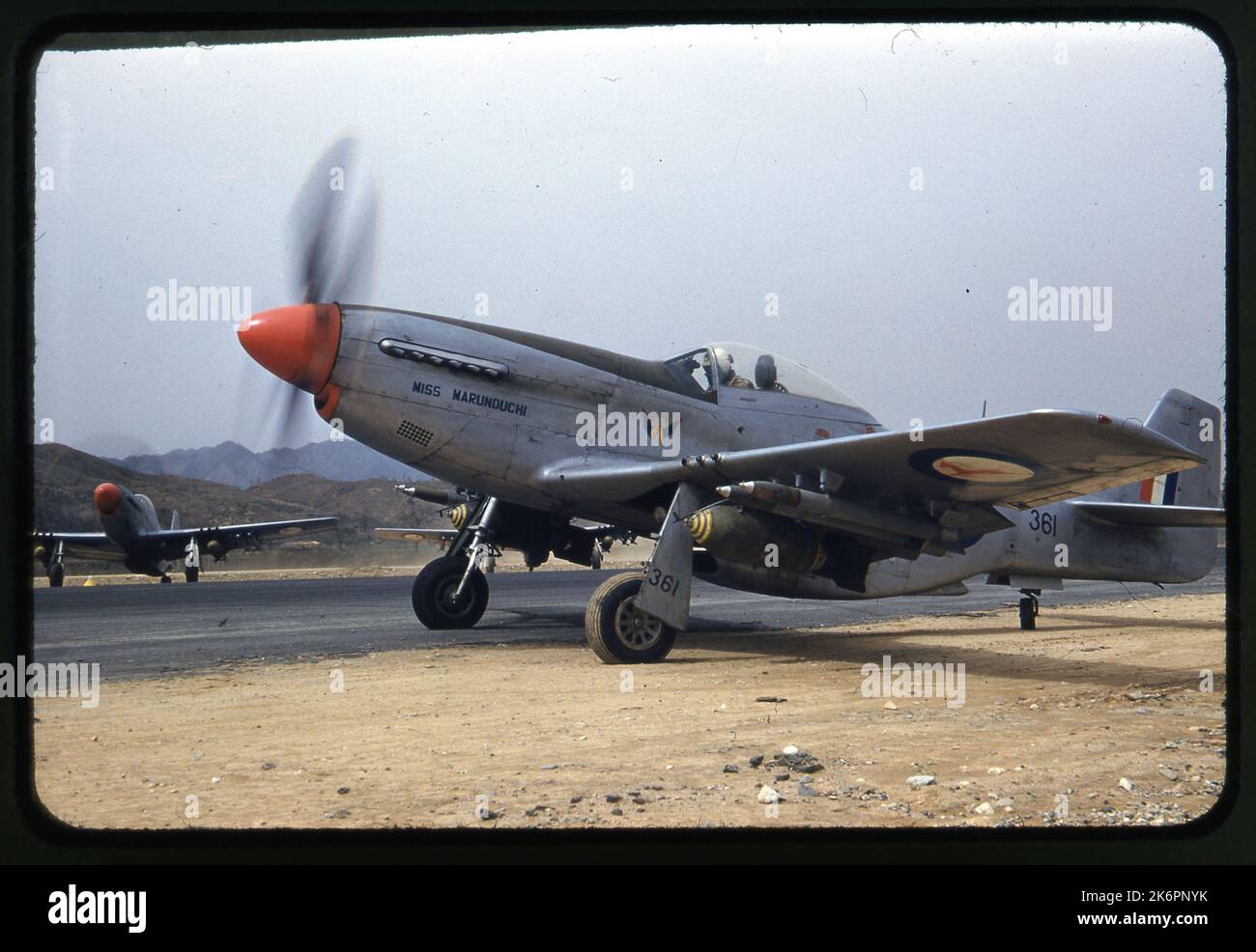 Un quarto della vista anteriore sinistra di un Mustang Mk nordamericano. IVA 'Miss Marunouchi' (s/n KM361) parcheggiata accanto alla pista, da qualche parte in Corea. Sullo sfondo, altri due Mustang Mk. IVS sono visibili. Ogni aeromobile porta le marcature dello Squadrone del 2nd dell'aeronautica sudafricana ed è armato di due bombe e quattro razzi. Foto Stock