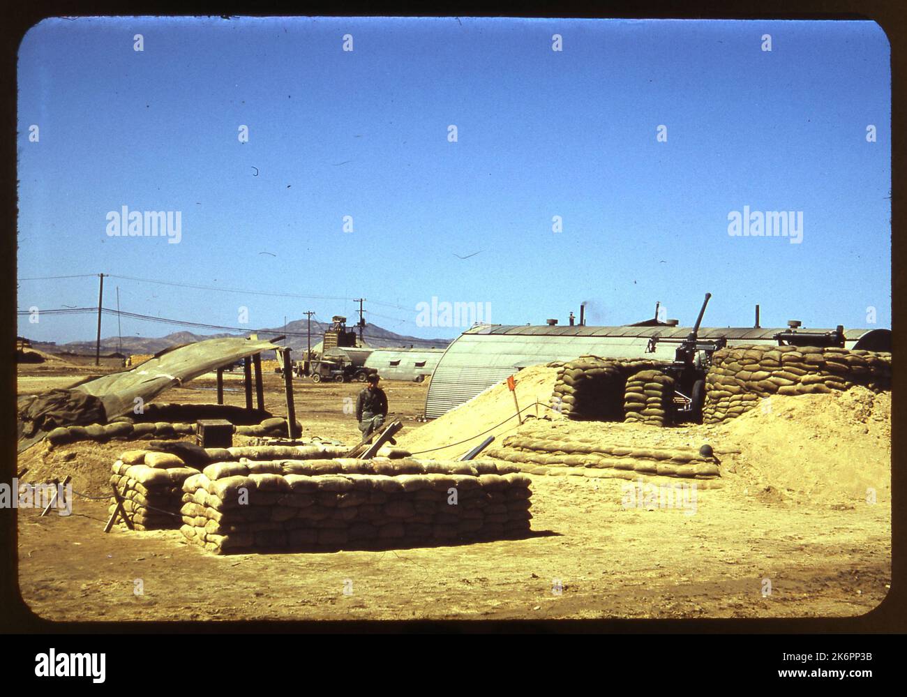 Vista posteriore a metà destra di una pistola antiaerea Bofors da 40 mm in un involucro sabbiato in un'aerbase in Corea. Le capanne e i veicoli di Quesonce appaiono sullo sfondo. Foto Stock