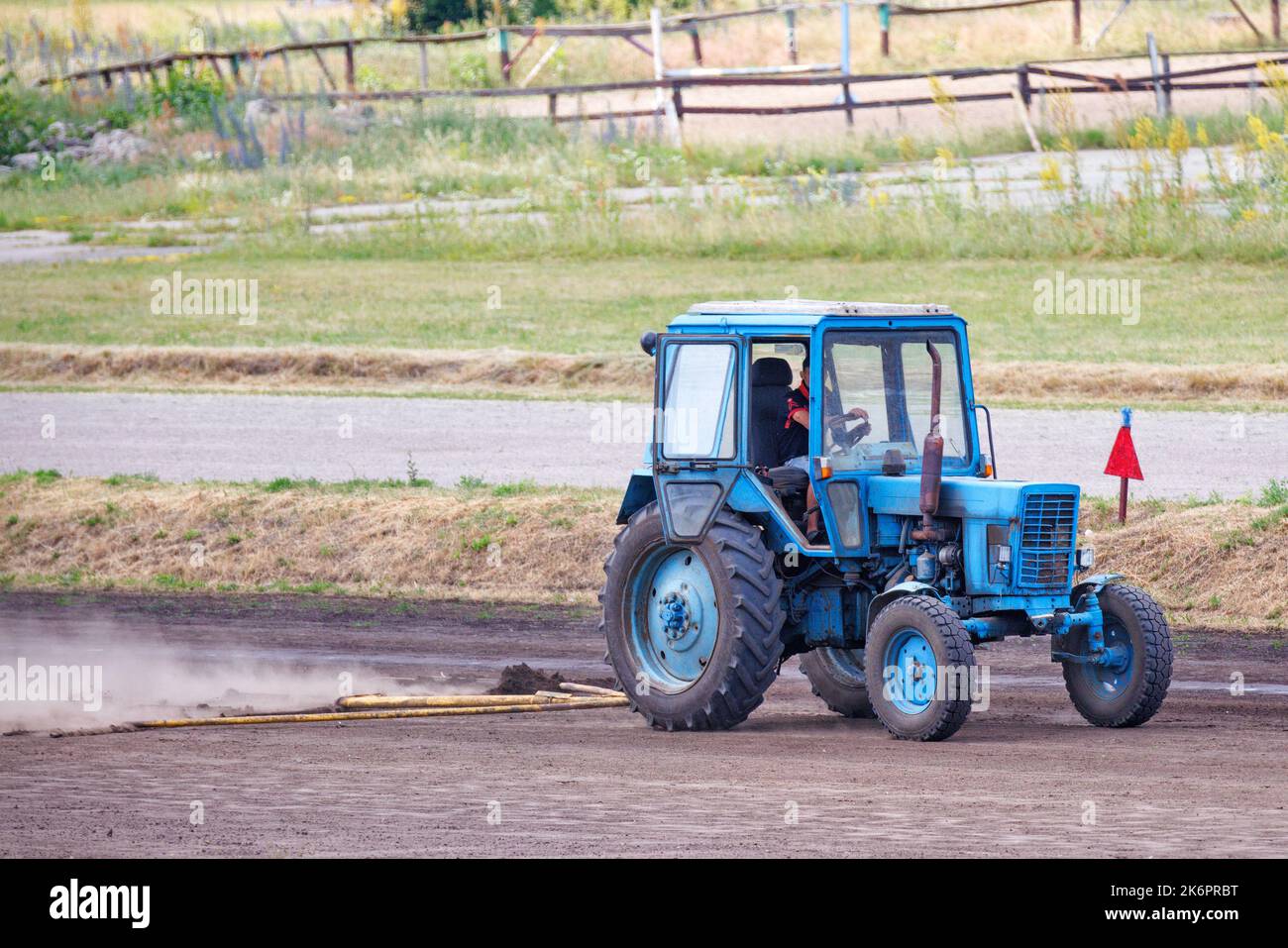 Un vecchio trattore blu livella la pista dell'ippodrome in una giornata estiva. Foto Stock