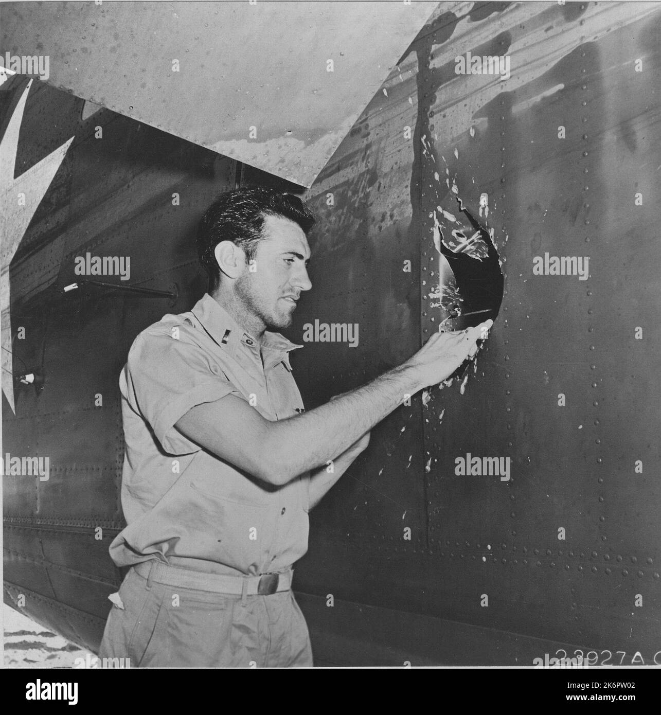 Fotografia del Lt. Louis Zamperini, ex membro della squadra NCAA (National Collegiate Athletic Association) Miler e Olympic, Bombardier, sull'aereo del Lt. Russel A. Phillips, che esamina il buco di shell esplosivo giapponese di 20 mm sul lato della fusoliera. Fotografia del Lt. Louis Zamperini, ex membro della squadra NCAA (National Collegiate Athletic Association) Miler e Olympic, Bombardier, sull'aereo del Lt. Russel A. Phillips, che esamina il buco di shell esplosivo giapponese di 20 mm sul lato della fusoliera. War Theatre #23 (Funafuti, Ellice Island) aerei, danni da battaglia. 1943-01-01T00:00:00. Foto Stock