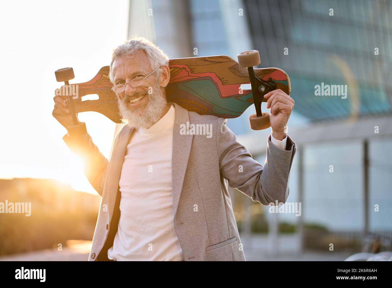 Felice cool anziano uomo d'affari anziano skater che tiene lo skateboard in città. Foto Stock