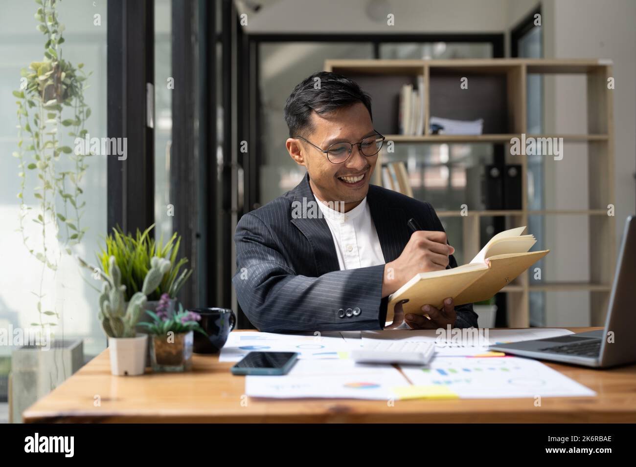 Uomo asiatico in tuta utilizzando il laptop e prendendo nota di scrivere lavorando per la finanza contabilità aziendale. Foto Stock