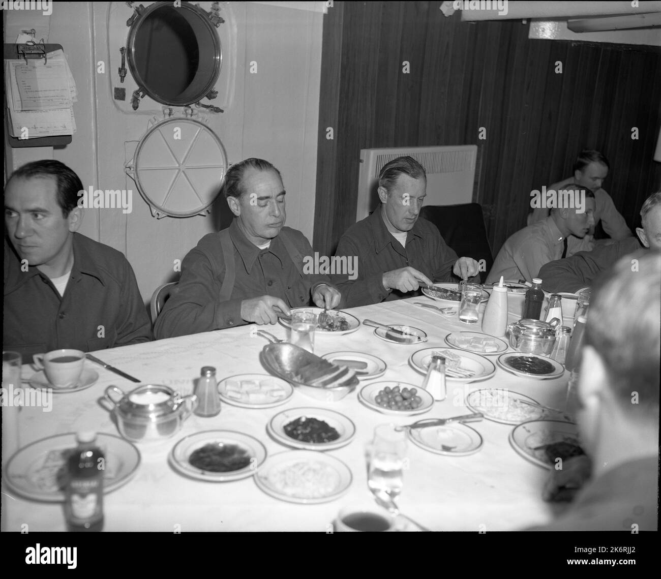 Photogrpah ha assunto la USS Atka (AGB-3). (Da sinistra a destra) H.J. Van Vuuren, dell'Ambasciata del Sud America, Washington, DC, Alan Moorhaed e Sidney Nolan cenano a bordo dell'ICE Breaker USS Atka (AGB-3) mentre operano nel Mare di Ross. Gli uomini sono ospiti dell'Ammiraglio posteriore James R. Reedy, Comandante degli Stati Uniti Naval Support Force, Antartide. Foto Stock