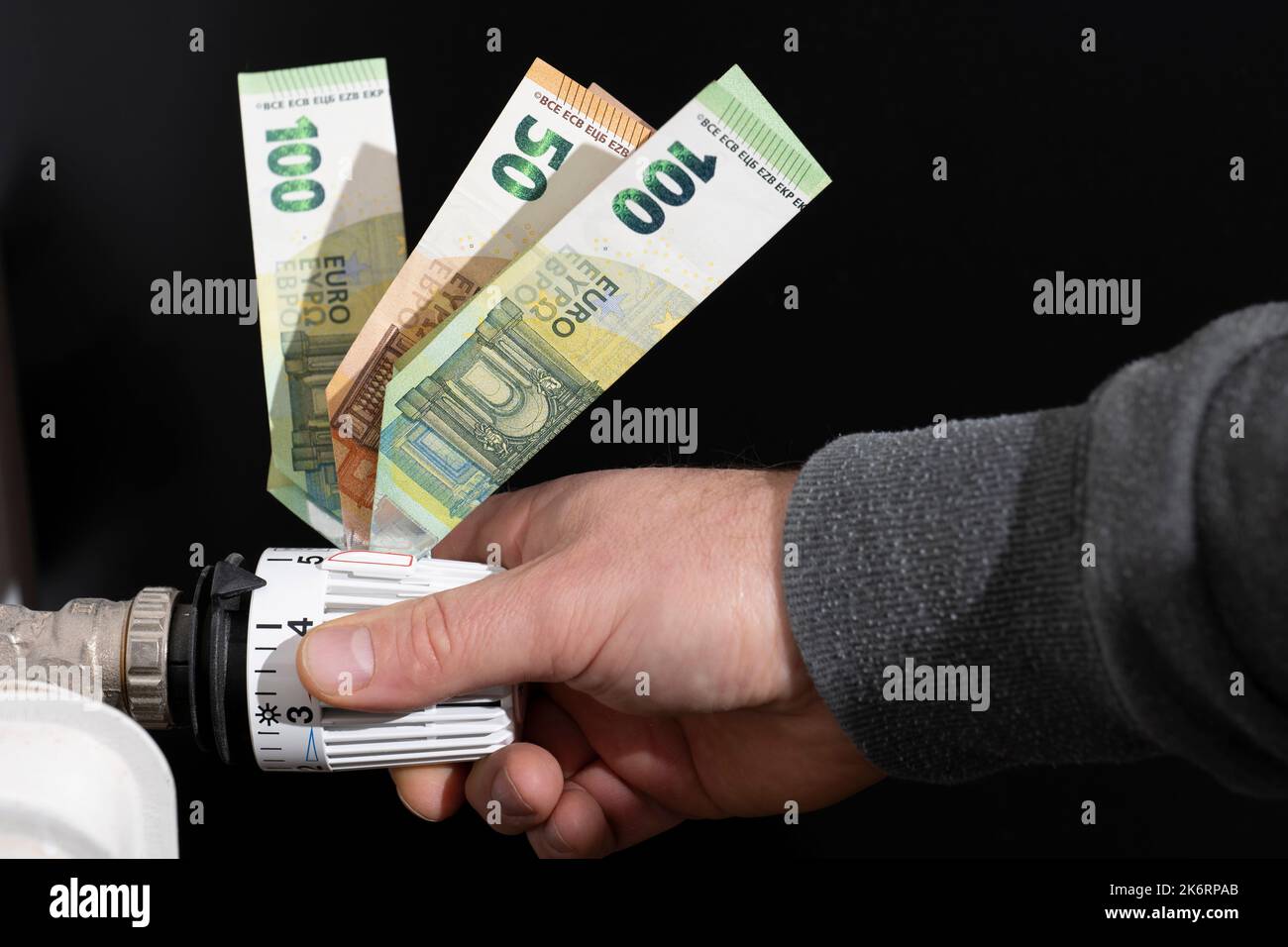 Il termostato di riscaldamento, dotato di banconote in euro, è regolato dalle mani degli uomini Foto Stock