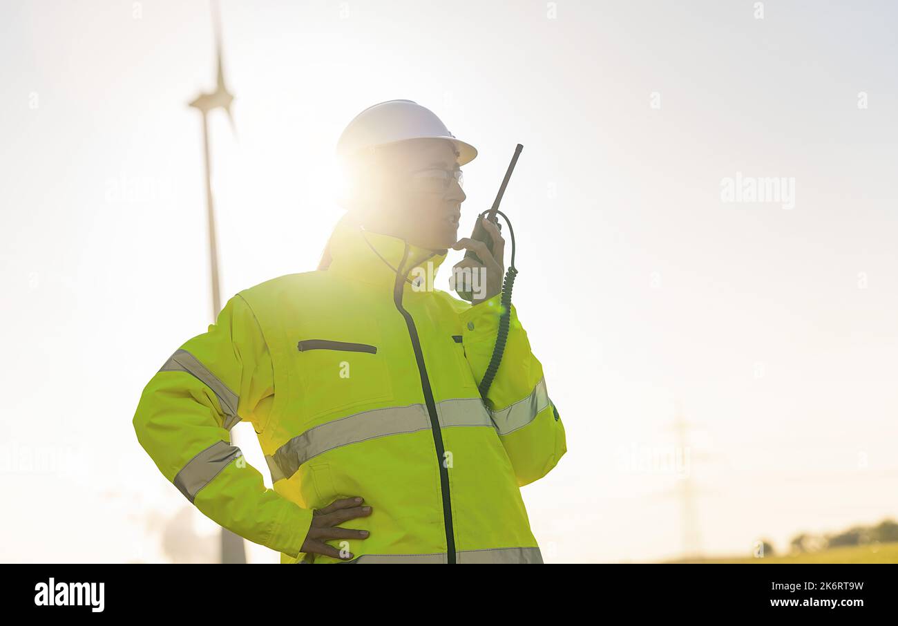 ingegnere donna con giacca di sicurezza utilizzando walkie talkie per il controllo del sistema di turbine eoliche in una nuova fattoria enegry Foto Stock