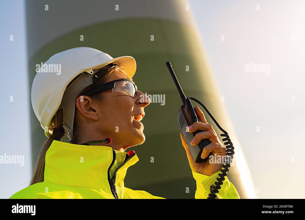 ingegnere donna con giacca di sicurezza utilizzando walkie talkie per controllare il sistema di turbine eoliche presso la centrale eolica Foto Stock